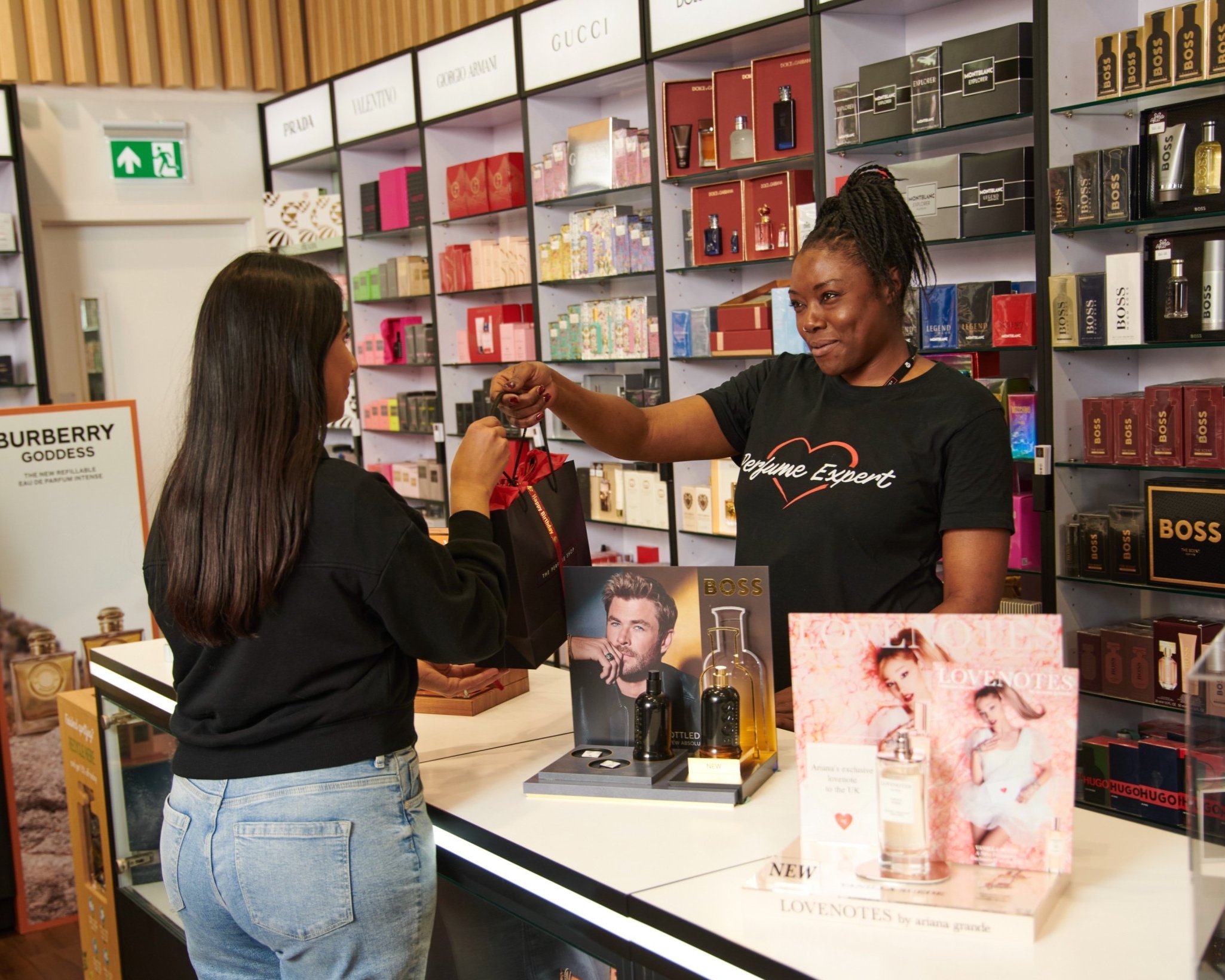 A customer receiving a gift bag from a perfume expert at a store.