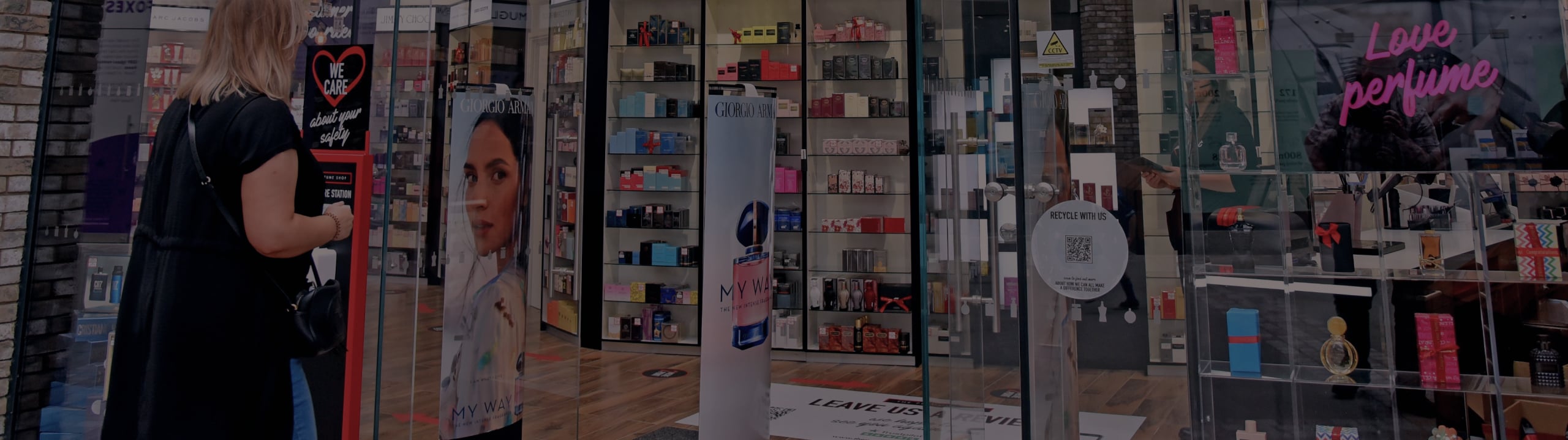 Woman looking at perfume shop with glass doors and shelves of fragrances.