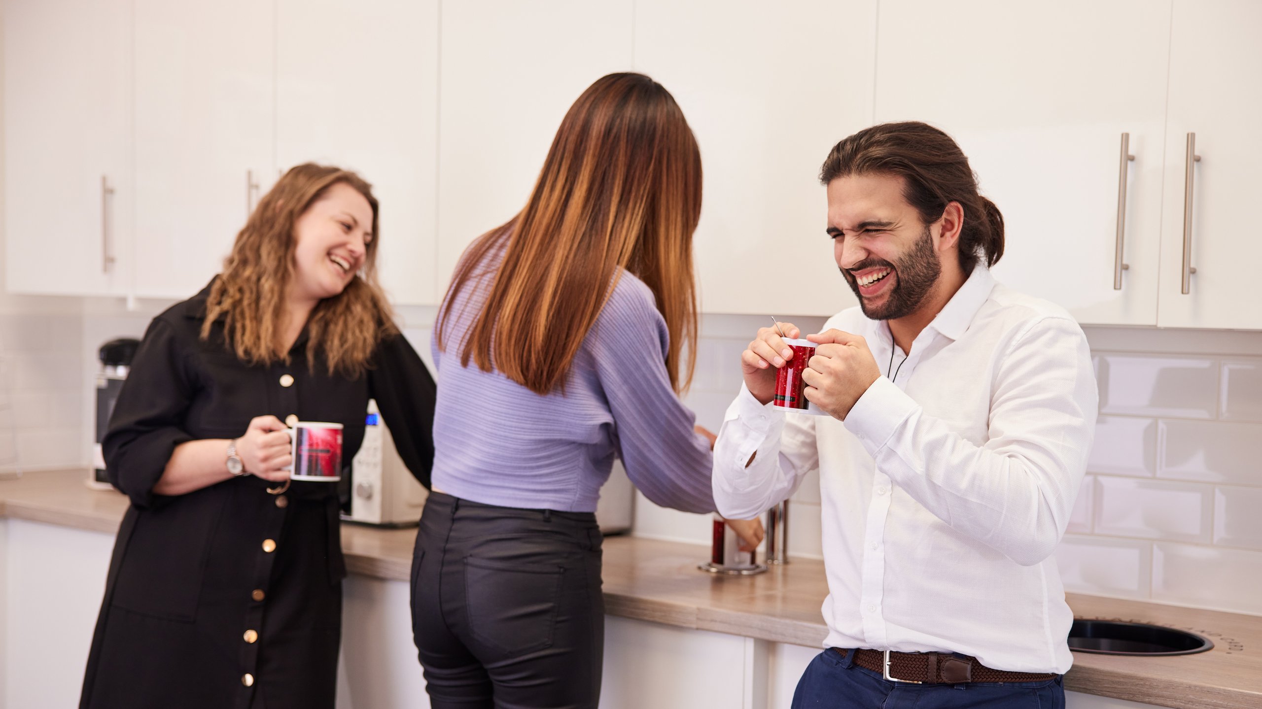 People gathered laughing in a kitchen, with drinks in hand.