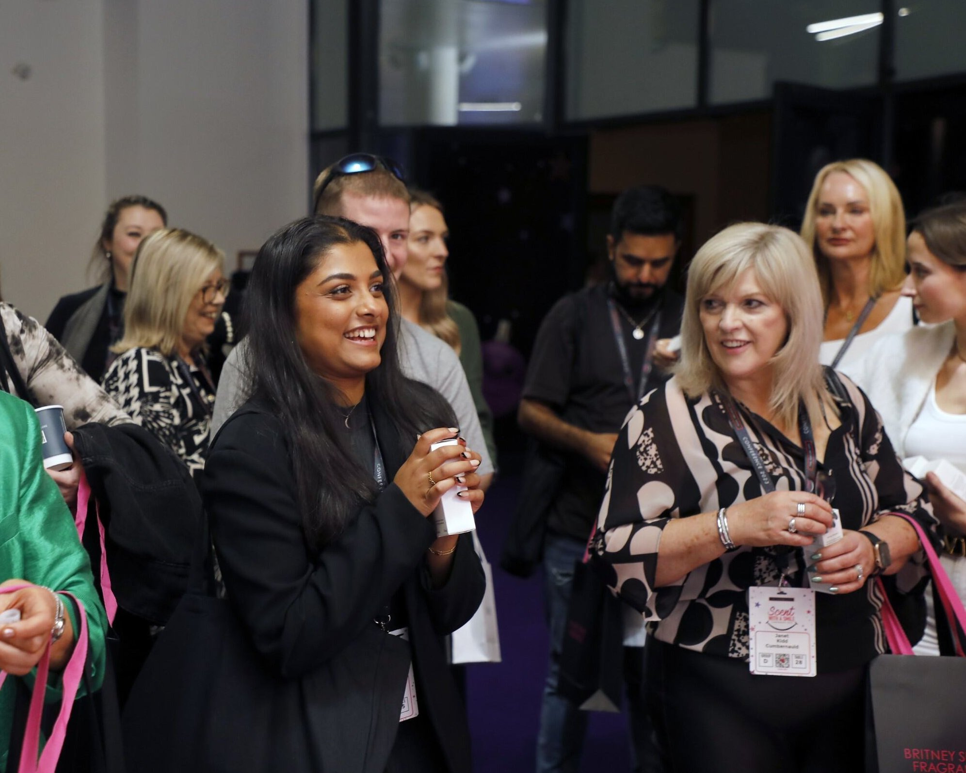 People smiling at a fragrance convention with name tags and bags.
