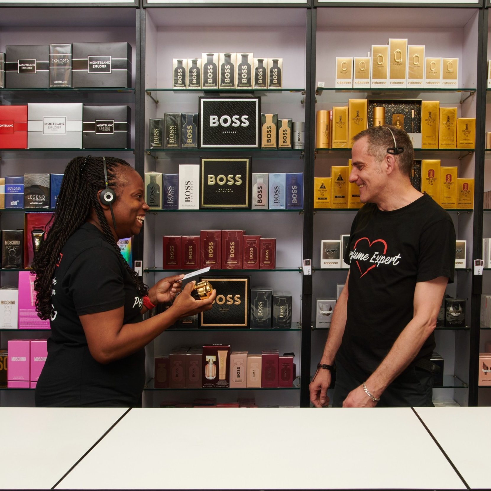 Two sales advisors in a perfume shop, with a display of various fragrances.
