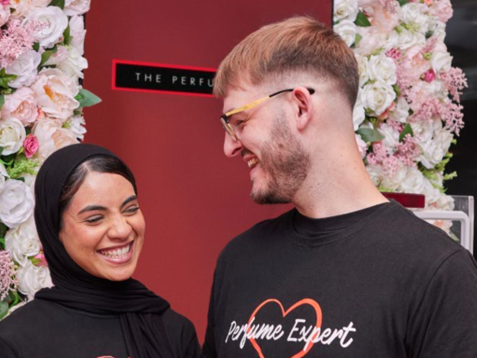 Two people wearing "Perfume Expert" shirts, smiling.