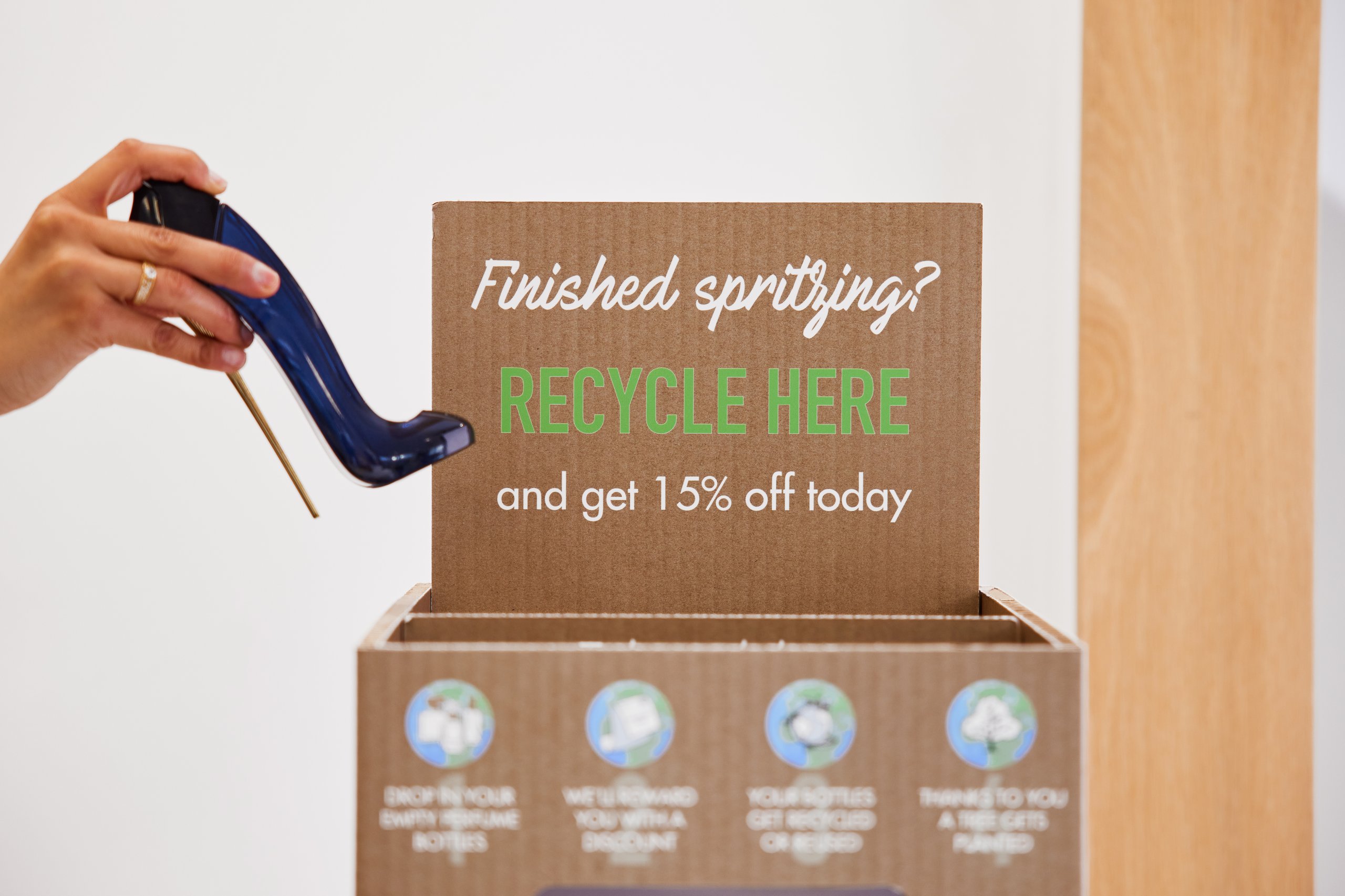 Woman with a perfume bottle near a recycle bin with promotional offers.