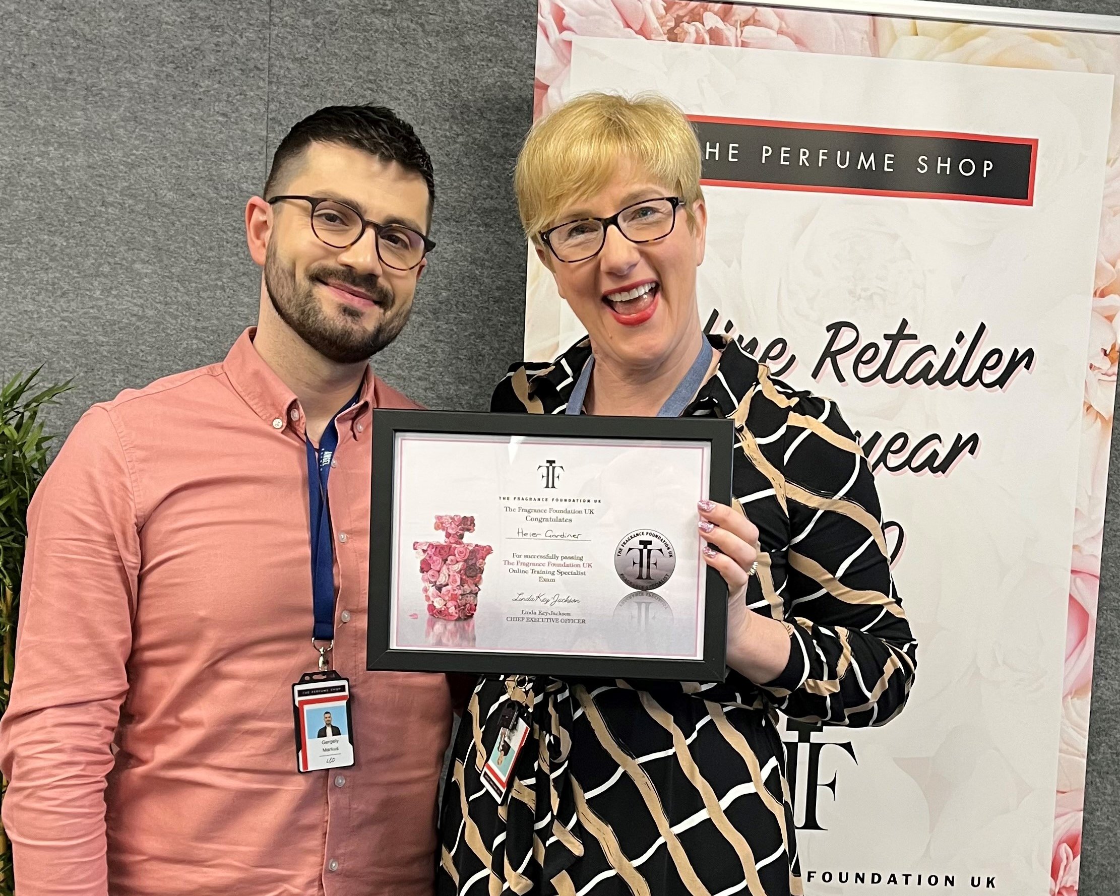 Two people holding award, Perfume Foundation UK. The Perfume Shop banner in the background.