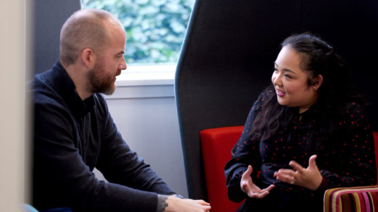 Two people in a conversation, seated in modern chairs.