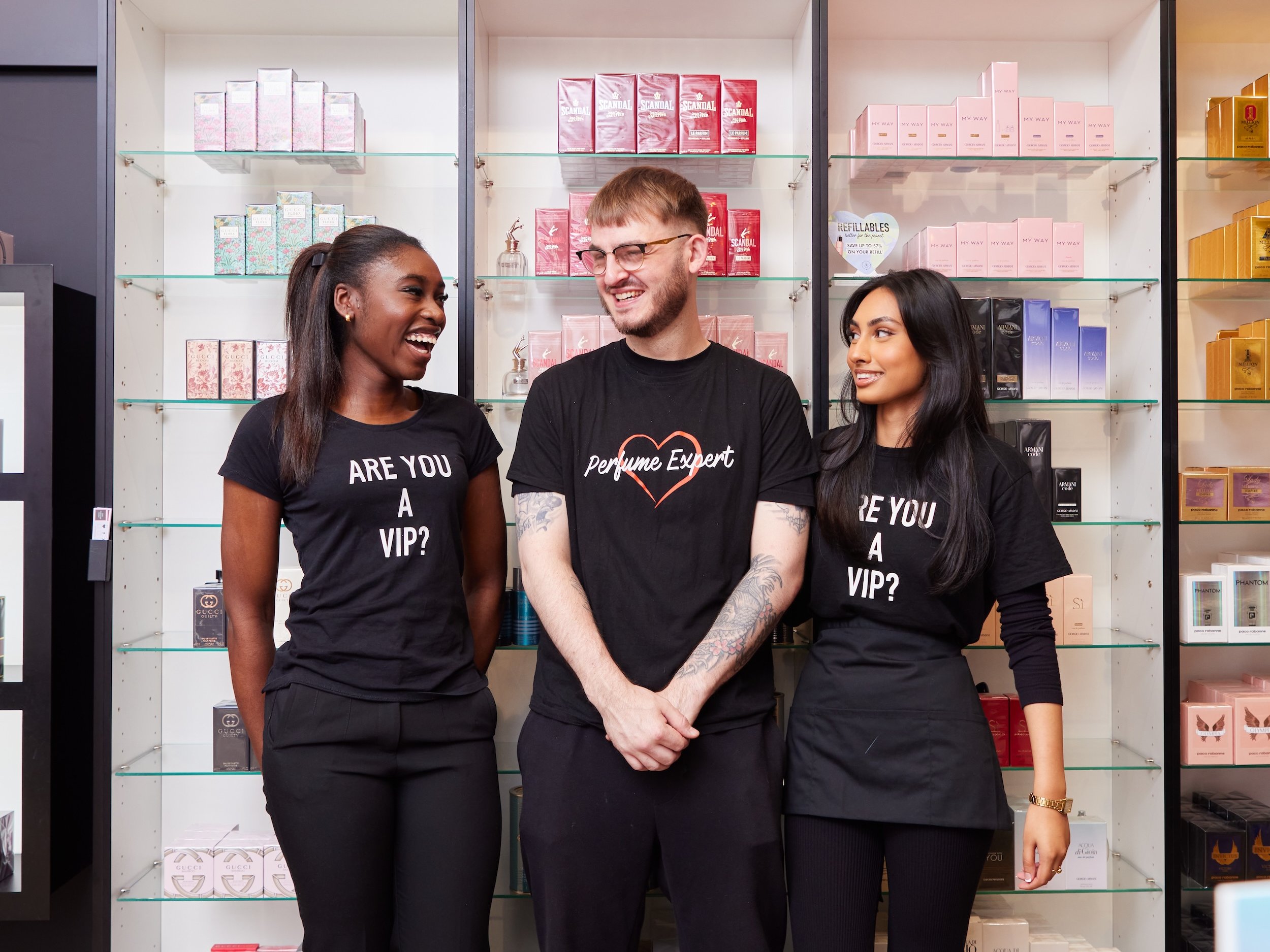 Three staff members in a perfume shop; shop display with perfumes in the background.