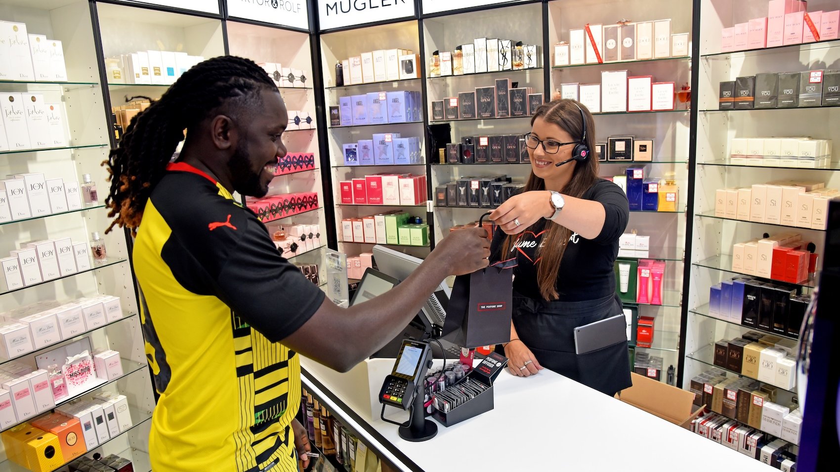 A customer receiving a shopping bag from a perfume shop employee.