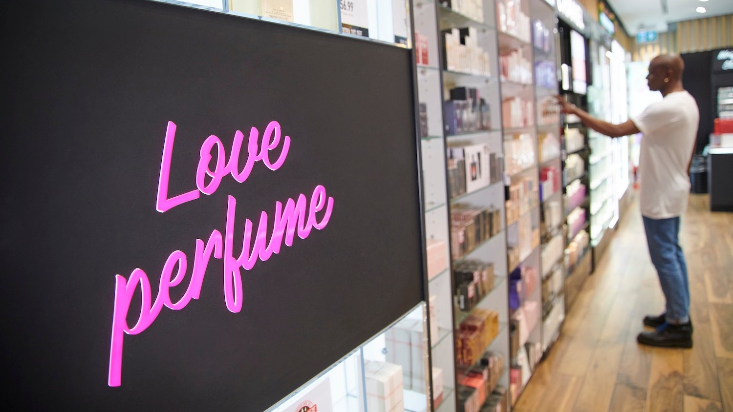 Man shopping in a perfume shop, shelves stocked with fragrances. "Love perfume" sign.