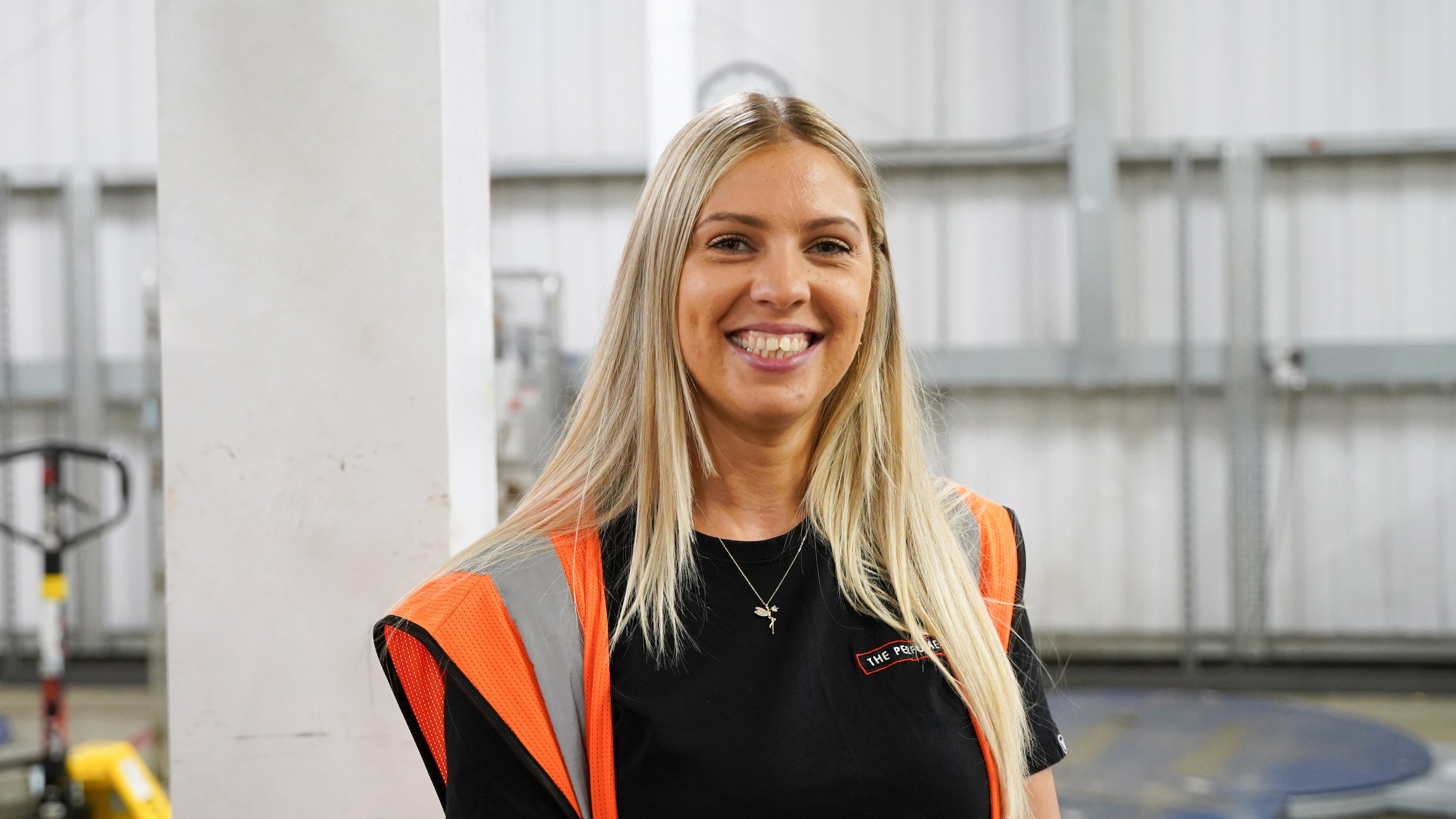 Woman wearing a safety vest and black t-shirt, smiling.