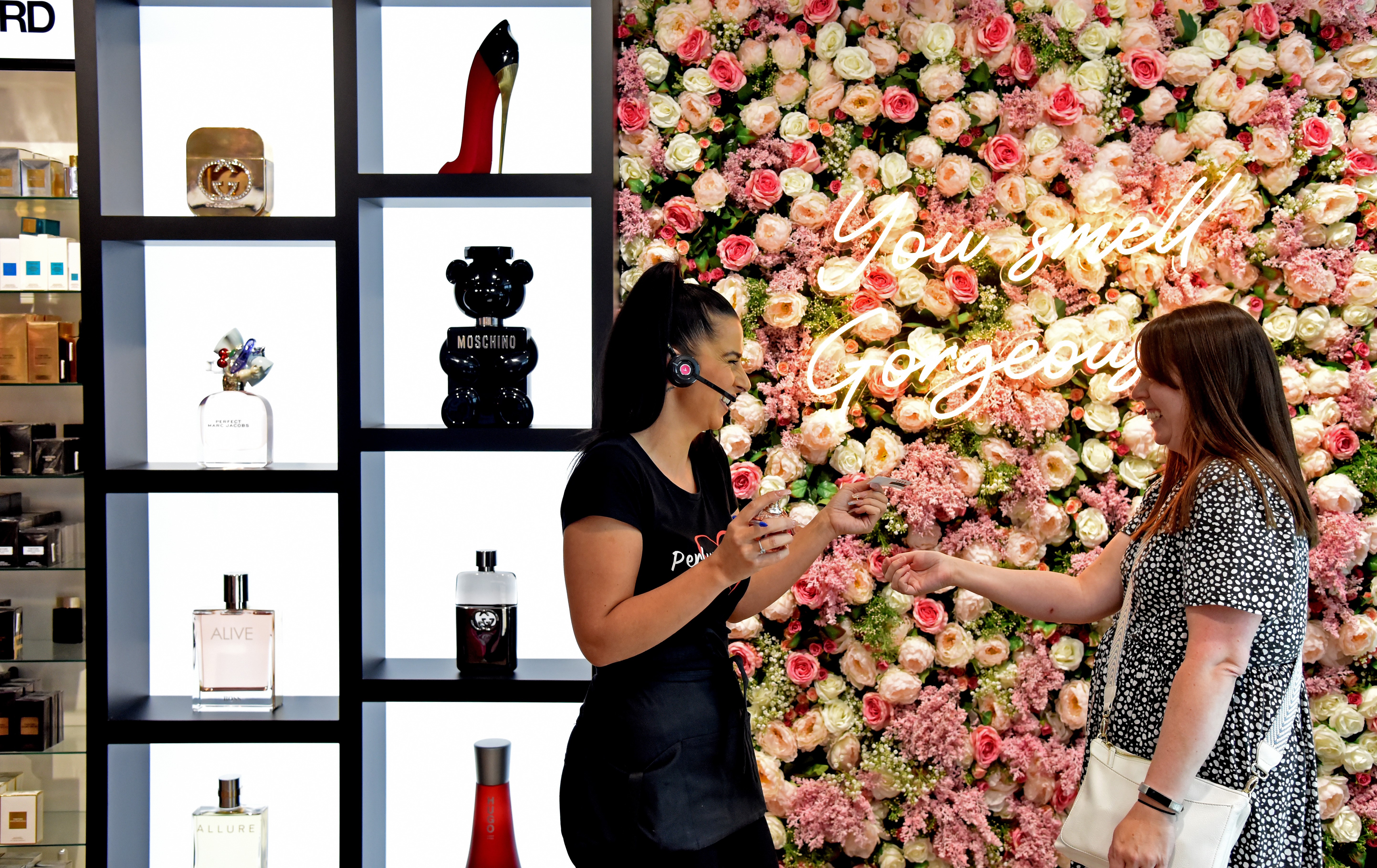 A perfume store employee assists a customer with a product sample.