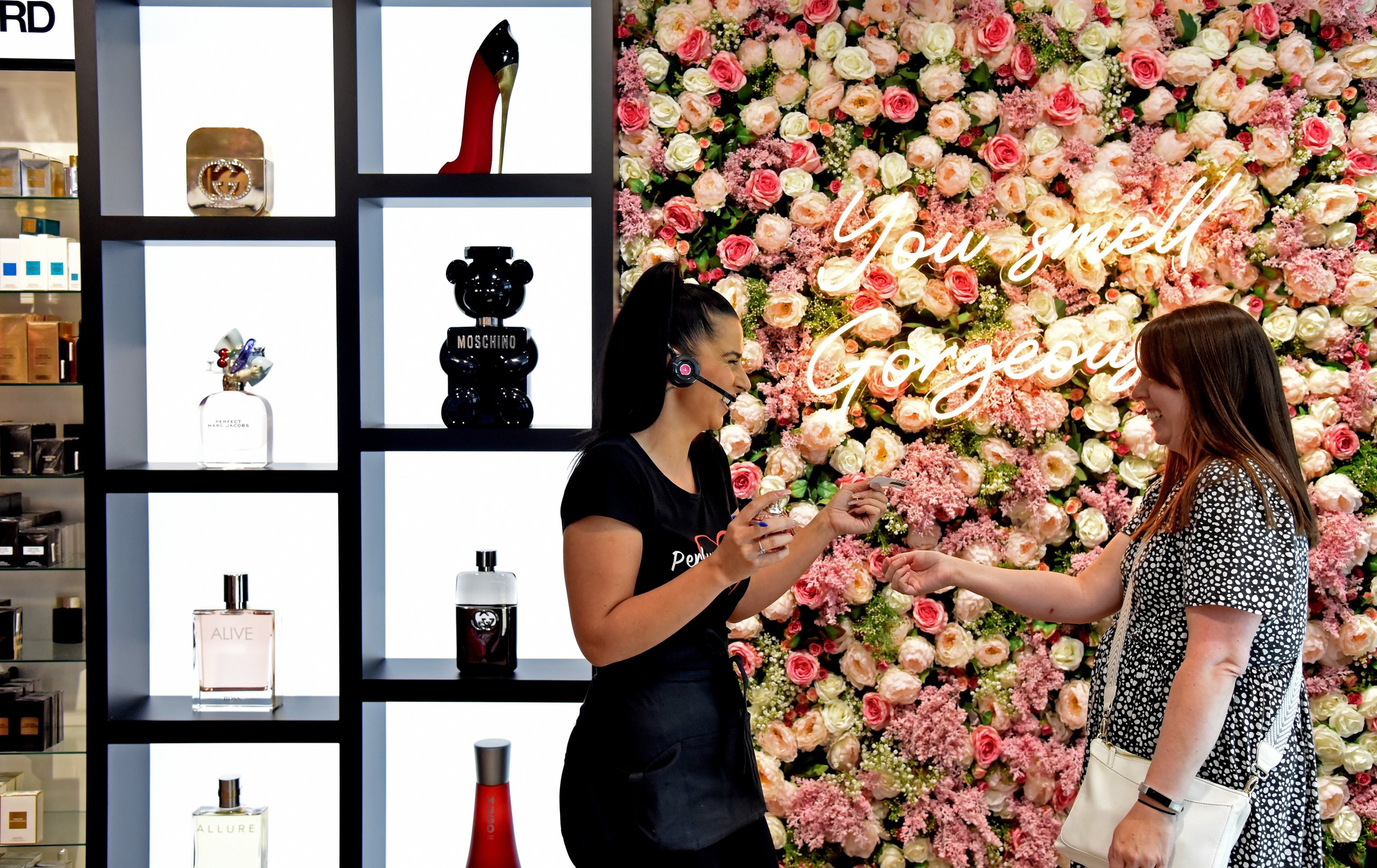 A perfume store employee assists a customer with a product sample.