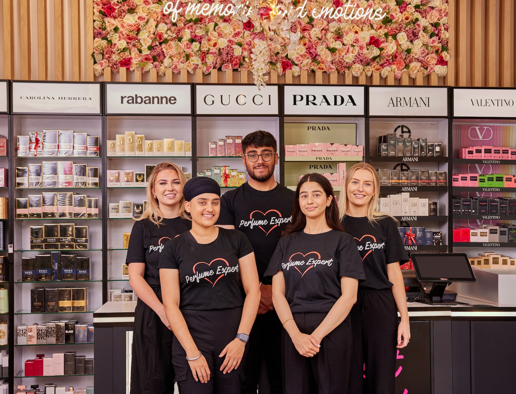 Staff of perfume store in front of brands display with floral wall decor.