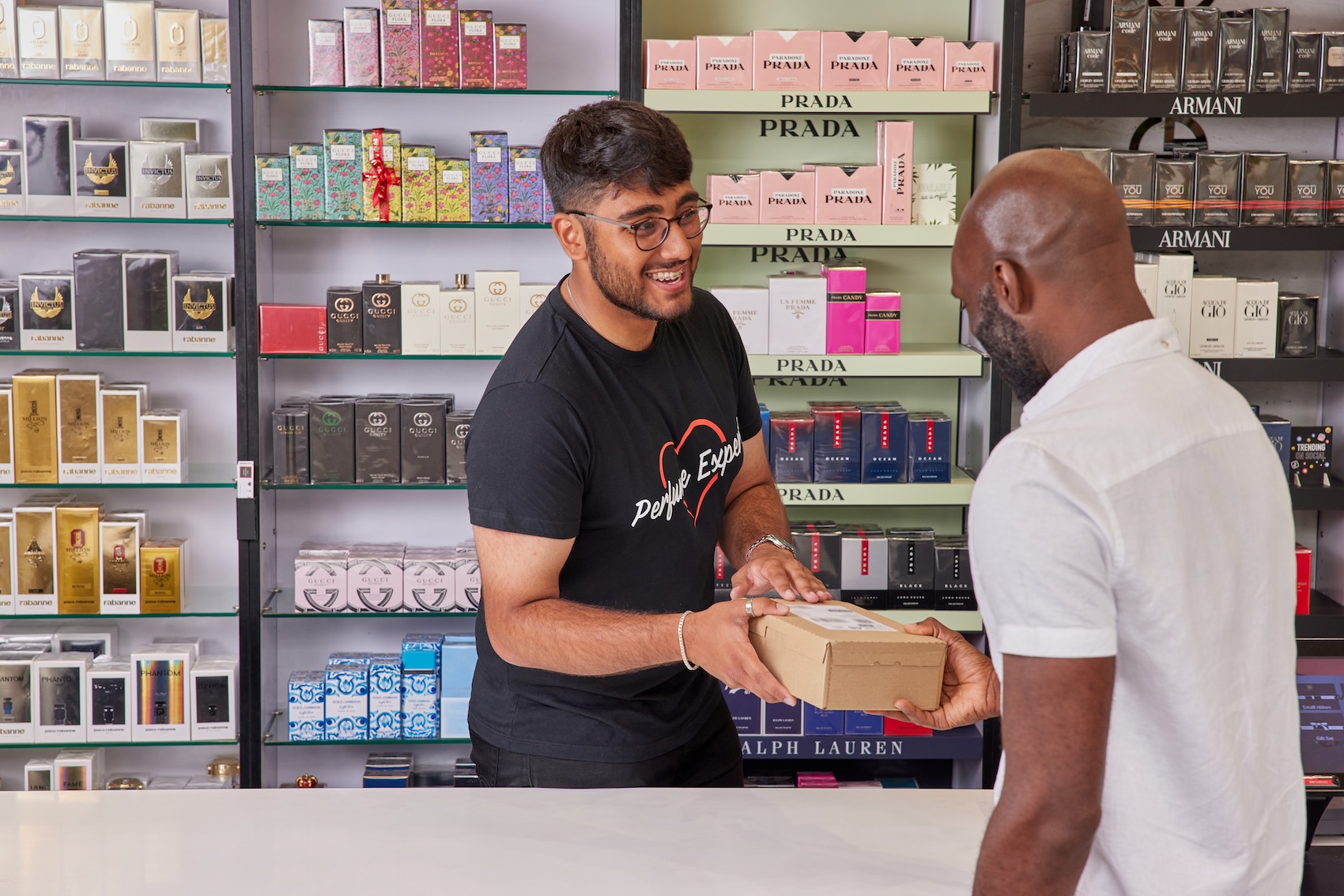 Man receiving a package from a store employee with perfume displayed.