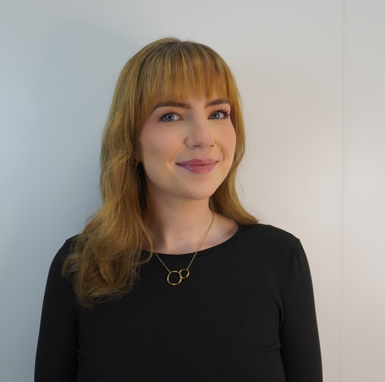 Portrait of a woman with blonde hair, wearing a black shirt, and a gold necklace.