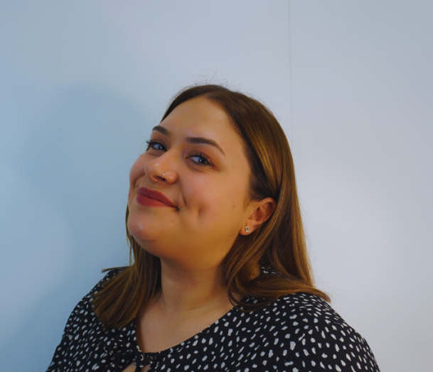 Woman smiling, wearing a polka dot top. She has dimples and a nose ring.