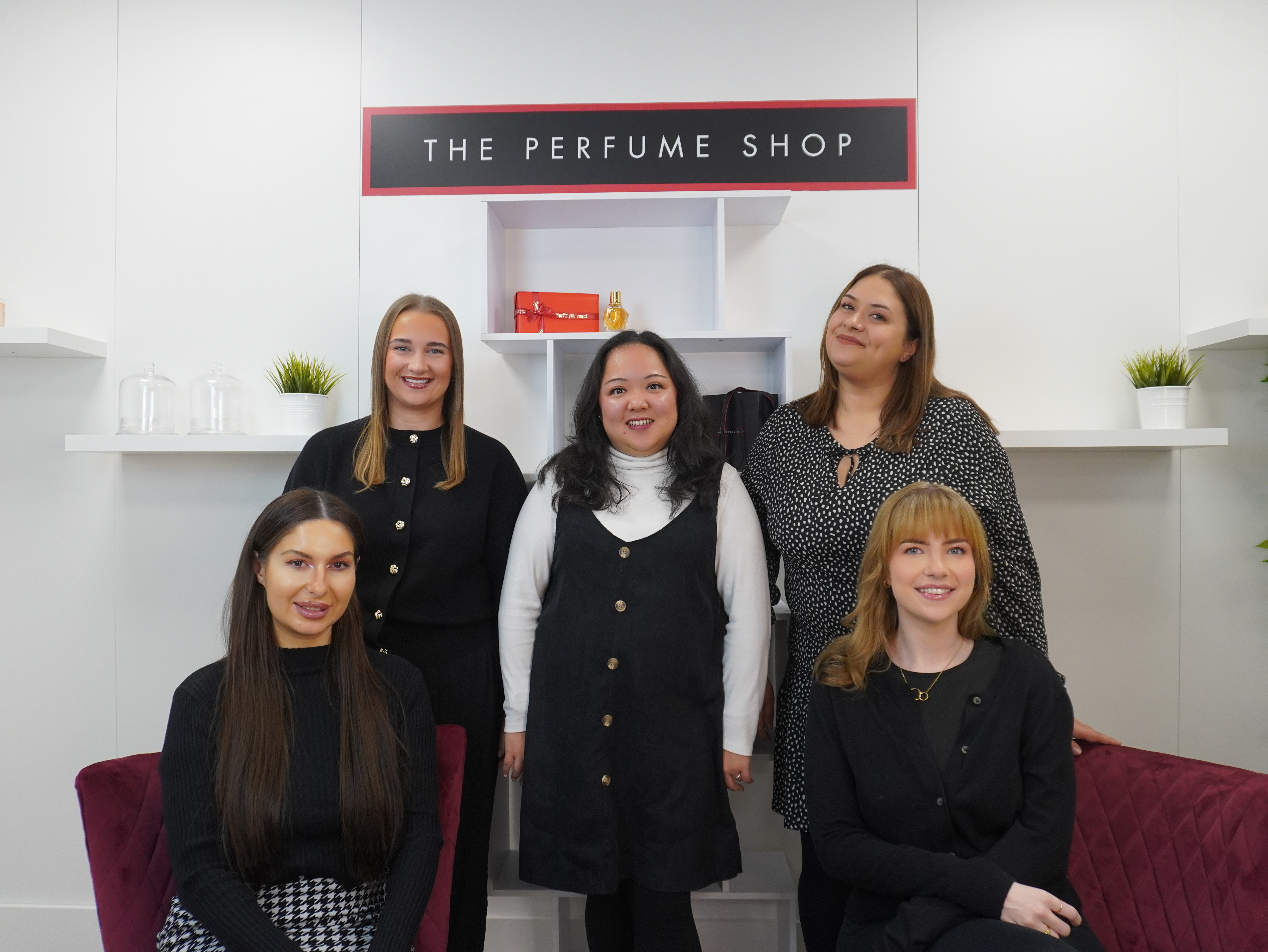Five women posing in front of "The Perfume Shop" sign.